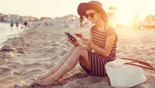 Junge Frau am Strand beim Online-Shopping mit Kreditkarte – Deutsche Assistance