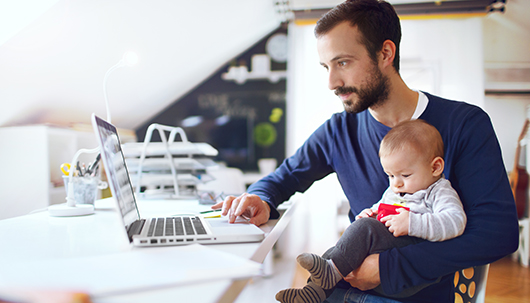 Vater mit Baby auf dem Schoß vor dem Laptop – Deutsche Assistance