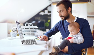 Vater mit Baby auf dem Schoß vor dem Laptop – Deutsche Assistance
