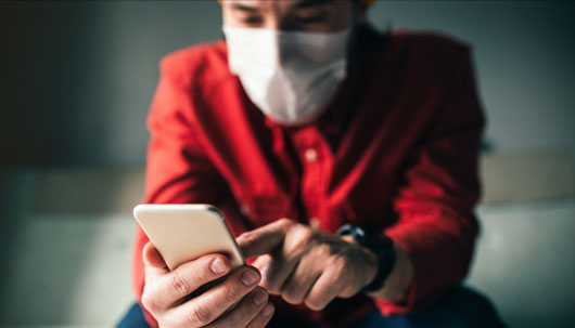 Kunde mit Atemmaske und Smartphone – Deutsche Assistance 