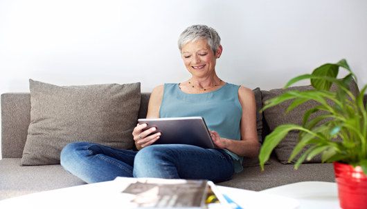 Cyberschutz-Kundin surft zu Hause auf der Couch mit Tablet im Internet - Deutsche Assistance 